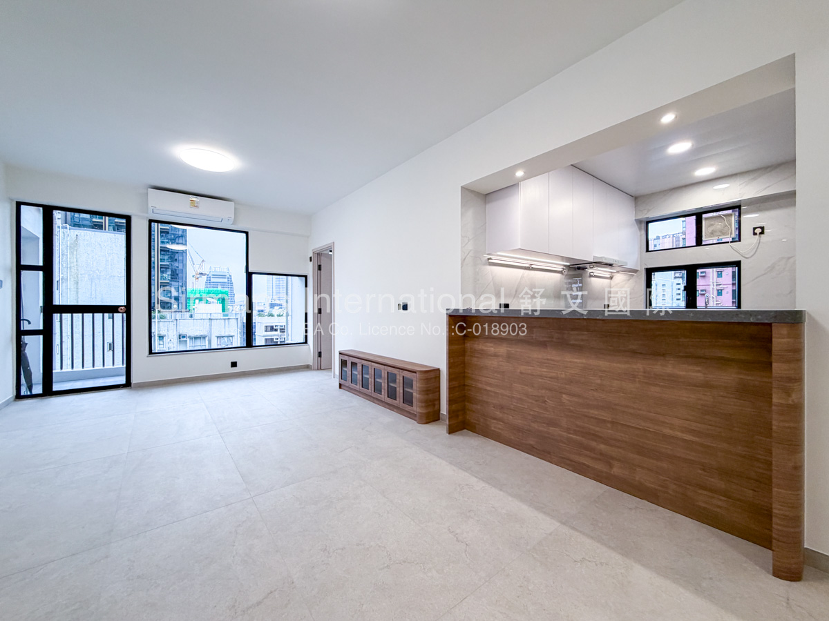 Vacant modern 2 bedrooms apartment interior with open-concept living area, abundant natural light from large windows offering urban city views, light gray porcelain floor tiles, minimalist white kitchen with wood-accent breakfast bar, and air-conditioning units