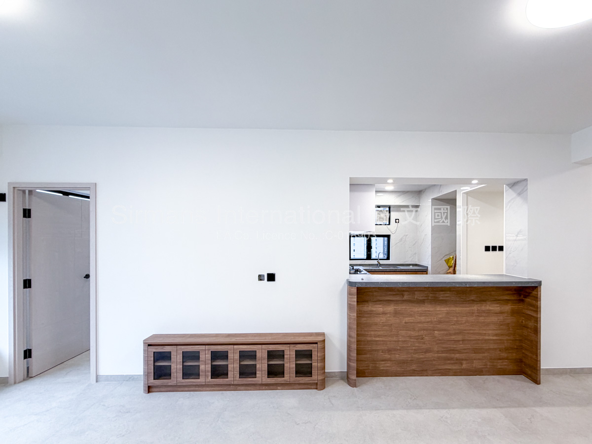 Empty bedroom in a newly renovated high-rise apartment, featuring light gray large-format porcelain floor tiles, crisp white walls, recessed ceiling lighting, a large black-framed corner window providing abundant natural light and direct views of surrounding urban high-rise buildings, a partially open light wood door leading to an en-suite or hallway, and a wall-mounted air-conditioning unit visible through the doorway.